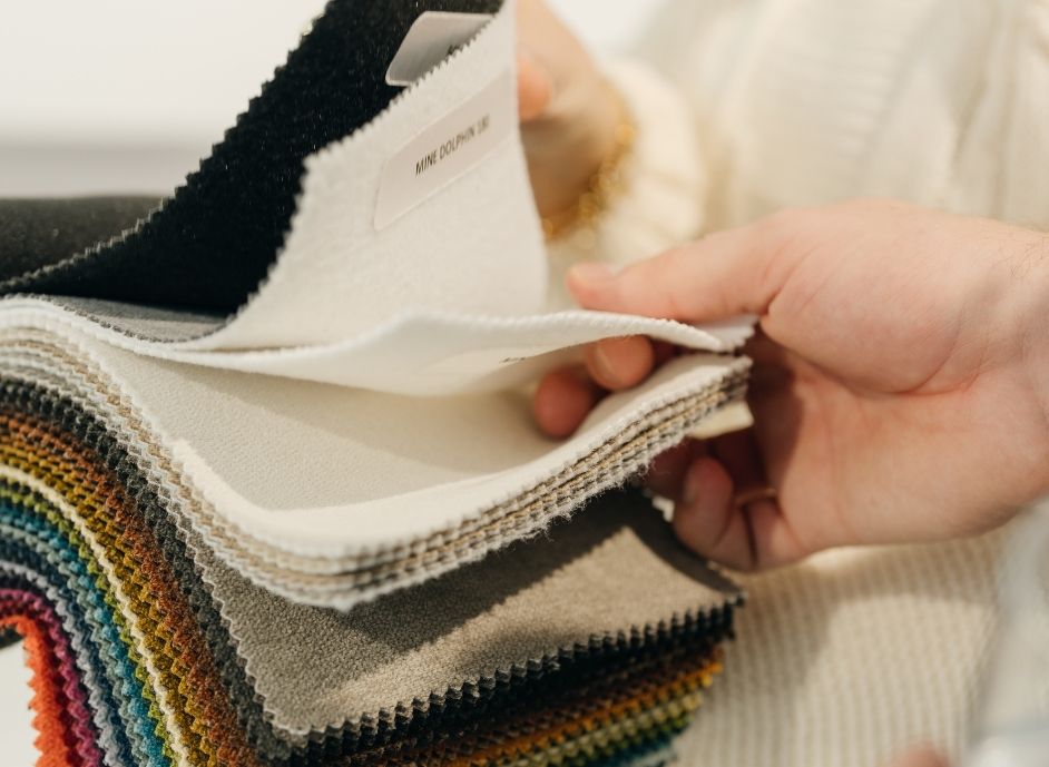 Hand blättert in einem Stoffmusterbuch mit verschiedenen Stoffproben in unterschiedlichen Farben und Texturen